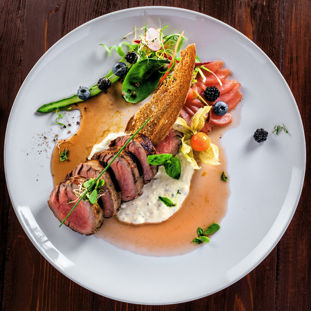 Medium rare meat steak medallions with sauce and salad on a plate. Delicious healthy food made of meat and vegetables for lunch. Top view.の写真素材