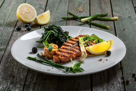 Grilled salmon fish steak with vegetable salad on a plate. Gourmet seafood meal made of fish and vegetables. Healthy food on a table.の写真素材