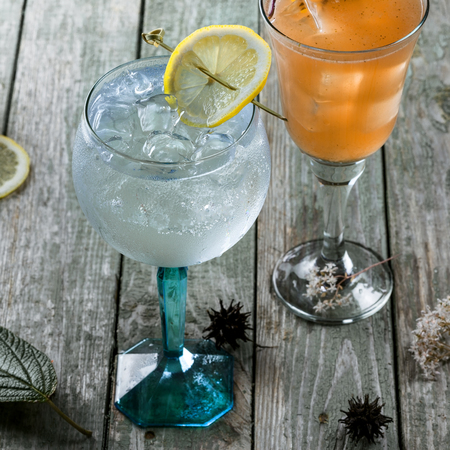 Alcoholic gin and tonic cocktail with drink made of rum, soda, ice and basil leaf in a long glass on a wooden table.の写真素材