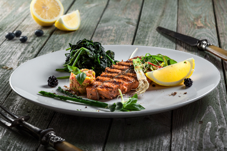 Grilled salmon fish steak with vegetable salad on a plate. Gourmet seafood meal made of fish and vegetables. Healthy food on a table.の写真素材
