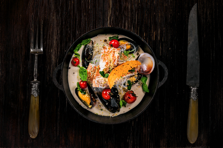 Seafood meal made of sea bass fish, mussels, crab meat and cockles with vegetables and rice noodles in delicious cream sauce in a black bowl. Top view.の写真素材