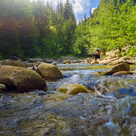Two tourists are fetching water from mountain river in summer Carpathians. Landscape of forest stream in mountains with people.の写真素材