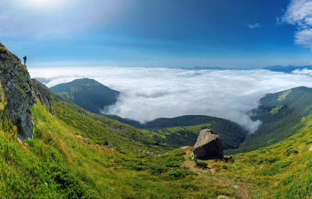 Panorama sunny landscape of Carpathian Mountains with a person on a rock. Tourist observing scenery from a top of a mountain.の写真素材