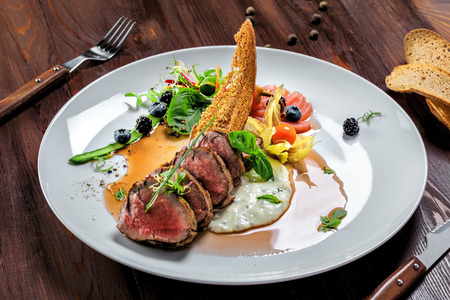 Gourmet medium rare meat steak with sauce and fresh salad. Healthy meal made of meat fillet and fresh vegetables on a rustic table.の写真素材