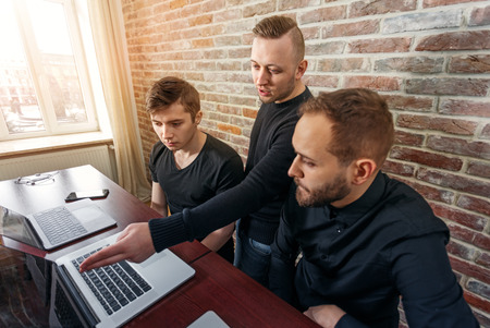 Team of three young men working in the office. Team of programmers looking for creative decision directed by team leader.の写真素材