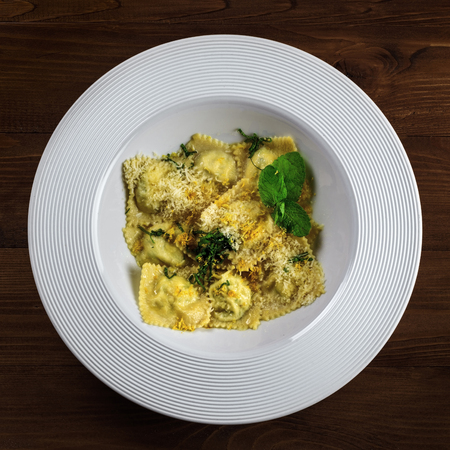 Ravioli filled with ricotta, mint and grated lemon rind on a rustic wooden table. Classic Italian cuisine pasta meal in a soup plate. Top view shot.の写真素材