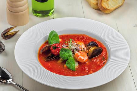 Excellent soup made of tomato and seafood on a rustic wooden table. Plate of healthy Italian meal.の写真素材