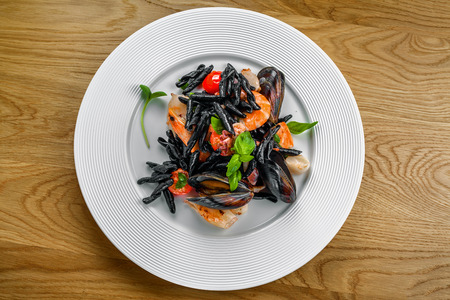 Excellent strozzaperti black squid ink pasta with seafood on a table. Plate of healthy Italian meal with shrimp, mussels and octopus. Top view, directly above shot.の写真素材