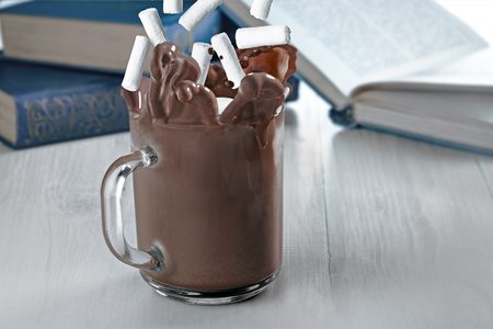 Cocoa splash made by dropped marshmellow in a transparent glass on awooden table with books.の写真素材