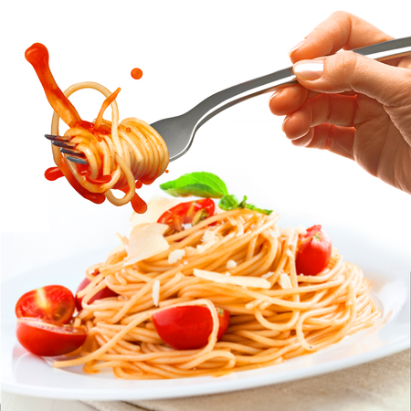 Female hand holds a fork with spaghetti and splash of tomato sauce over the plate with pasta and parmesan.の写真素材