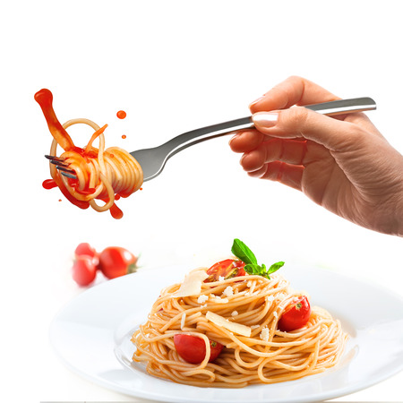 Female hand holds a fork with spaghetti and splash of tomato sauce over the plate with pasta and parmesan.の写真素材