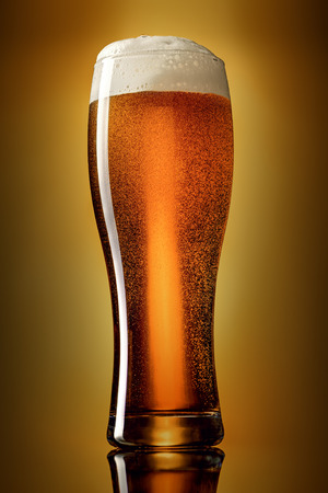 Glass of classic lager beer on gradient yellow to brown background. Studio shot.の写真素材