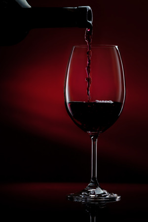 Red wine being poured in a wine glass on a dark red gradient background. Studio close-up shot.の写真素材