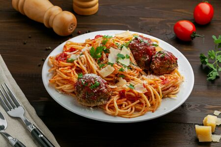 Delicious spaghetti pasta with meatballs and tomato sauce on a plate. Traditional American Italian food on a rustic wooden table.の写真素材