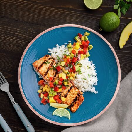 Grilled fillet of salmon with rice garnish and exotic fruit sauce made of mango, avocado, pepper and onion on a rustic table. Top view shot above.の写真素材