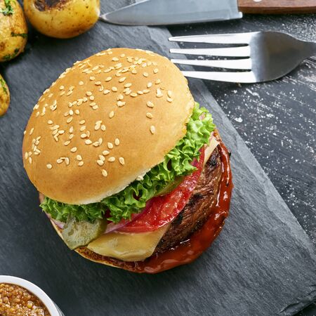 Hamburger with grilled vegetables and scallion served on a stone board and a glass of beer on a rustic black table. Top view, directly above.の写真素材