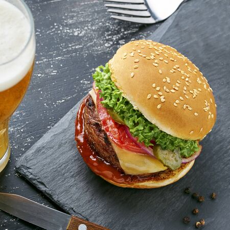 Delicious cheeseburger with baked potatoes and broccoli on a black stone board served with a glass of lager beer. Top view, directly above.の写真素材