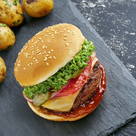Classic hamburger with tomato, lettuce and onion served with grilled potatoes and broccoli on a black stone board. Top view, directly above.の写真素材
