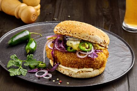 Chicken burger with vegetable salad and mayonnaise on a black plate. Gourmet sandwich with a glass of beerの写真素材