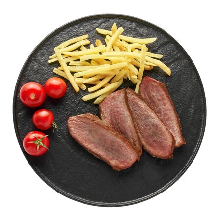 Delicious medium rare steak with French fries and fresh cherry tomatoes on a black plate. Classic meat meal isolated on white background. Top view, directly above shot.の写真素材