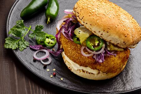 Homemade sandwich with chicken burger red onion, pickled cucumber, jalapeno and mayonnaise on a black pottery plate. Close-up shot.の写真素材
