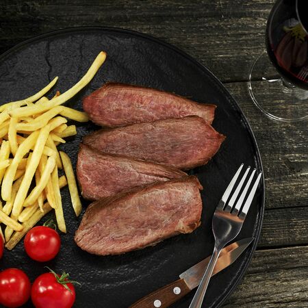 Gourmet medium rare beefsteak with French fries and fresh cherry tomatoes on a black plate served with red wine and sauce. Top view, directly above shot.の写真素材