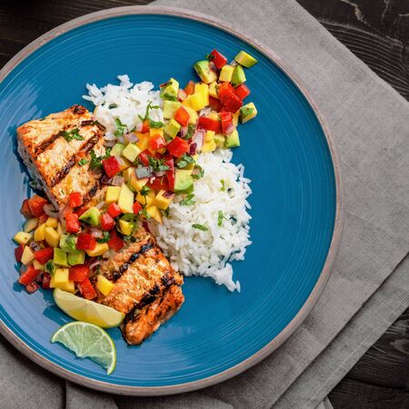 Delicious grilled salmon steak on a blue plate with jasmine rice and sauce made of mango, bell pepper, onion and avocado. Top notch food. Top view shot above.の写真素材