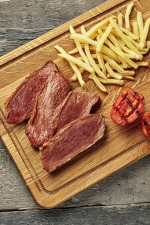 Steak with French fries and grilled cherry tomatoes on a cutting board. Classic meat meal with red wine on an ethnic tablecloth. Top view, directly above.の写真素材