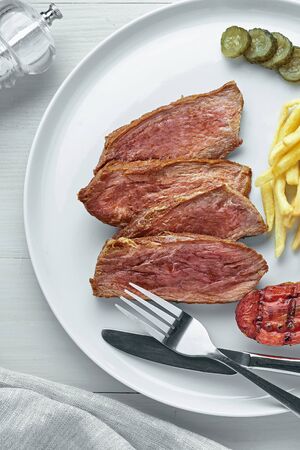 Medium rare sirloin steak with chips and a glass of sparkling water on a white wooden table with tablecloth. Classic European lunch. Top view, directly above.の写真素材