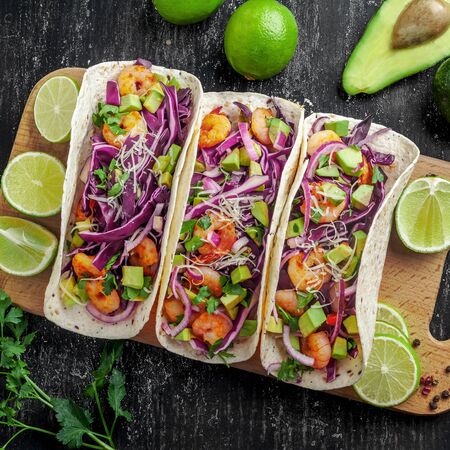 Delicious tacos with shrimps, avocado, onion and lime on a wooden board. Classic Tex-Mex cuisine meal. Top view shot, directly above.の写真素材