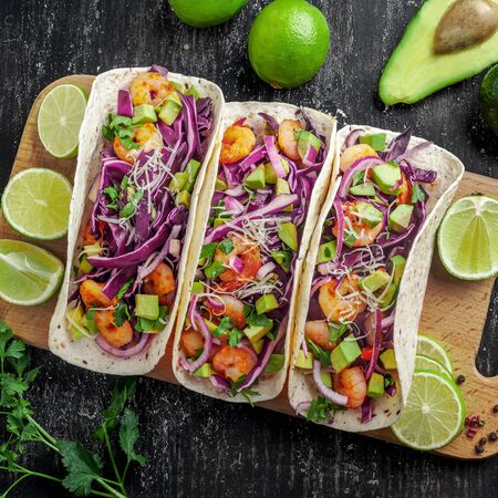 Delicious tacos with shrimps, avocado, onion and lime on a wooden board. Classic Tex-Mex cuisine meal. Top view shot, directly above.