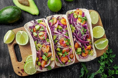 Delicious tacos with shrimps, avocado, onion and lime on a wooden board. Classic Tex-Mex cuisine meal. Top view shot, directly above.の写真素材