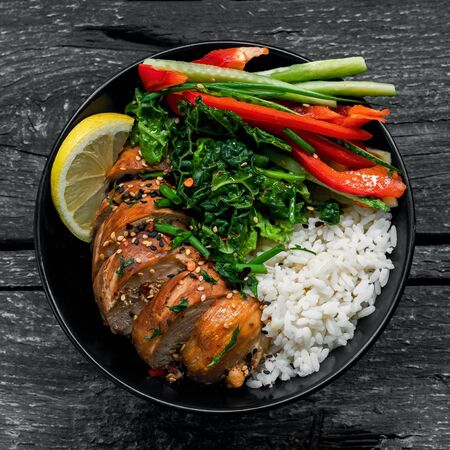 Buddha bowl meal with teriyaki chicken fillet, fresh vegetable salad, stew cabbage and basmati rice on a rustic table. Delicious dish in a black bowl. Top view, directly above shot.の写真素材
