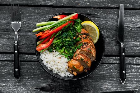 Lunch bowl with teriyaki chicken, cucumber, red bell pepper, green onion, stew spinach and basmati rice on a rustic black table. Top view, directly above shot.の写真素材