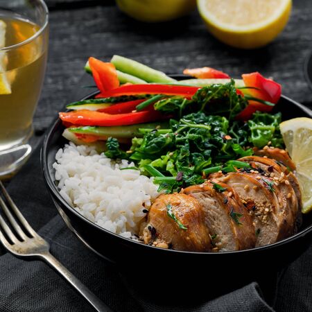 Buddha bowl meal with teriyaki chicken fillet, fresh vegetable salad, stew cabbage and basmati rice on a rustic table. Delicious dish in a black bowl with homemade lemonade.の写真素材