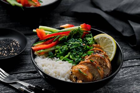 Two lunch bowls with teriyaki chicken, cucumber, red bell pepper, green onion, stew spinach and basmati rice on a rustic black table.の写真素材