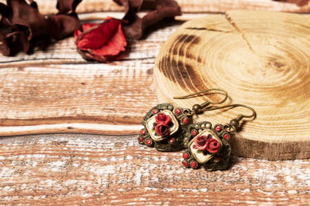 Retro earrings on wooden table, with wooden pad. Old fashioned earrings for women, with dark red roses.の写真素材