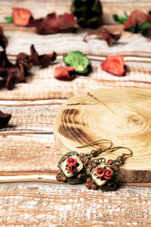 Retro earrings on wooden table, with wooden pad. Old fashioned earrings for women, with dark red roses.の写真素材