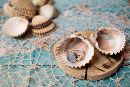 Beautiful golden ring with blue stone, in a seashell. Blue sea background, with sea net, seashells on a wooden pad.の写真素材