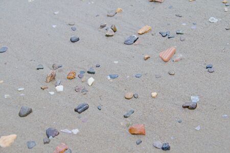 Photo shows a detail of the various stones on the sandy beach.の写真素材