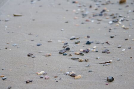 Photo shows a detail of the various stones on the sandy beach.の写真素材