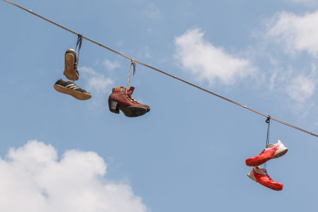 Photo shows close-up of waving old shoes on cable in summer.の写真素材