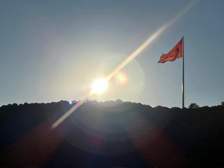 Red flag on top of a mountain with the sun in the backgroundの写真素材