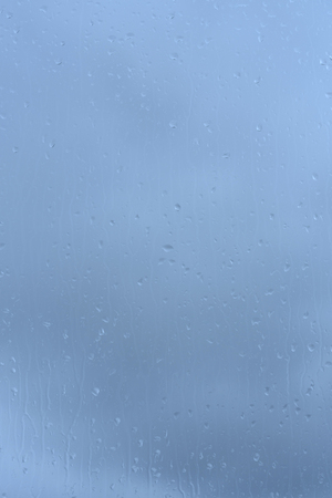Raindrops on glass, spectacular sky background with color effectの写真素材