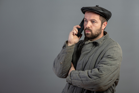 Serious caucasian man 35 years old speaks on mobile phone, studio shot. Idea - village dweller and modern technology, setの写真素材