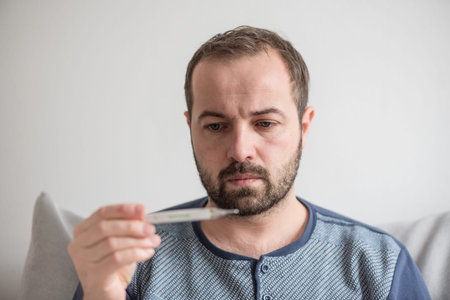 Sick man checks the body temperature with a mercury thermometer. Theme of viral diseases, flu,...