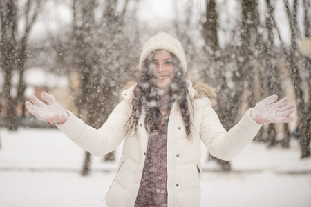 Young beautiful woman is enjoying the snow scattering it in the air, positive emotions, joy and happiness. Winter outdoor activities.の写真素材