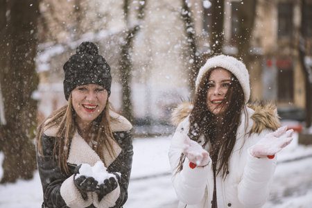 Young beautiful woman is enjoying the snow scattering it in the air. Winter outdoor activities,...