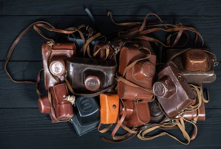 Drohobych, Ukraine - 02 February, 2019: Heap of 35mm retro cameras in leather covers on black, top viewのeditorial素材