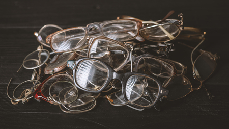 Heap of scratched and broken eyeglasses on black wooden boards, matte effect. Repairing and replacing old eyeglasses, eye careの写真素材